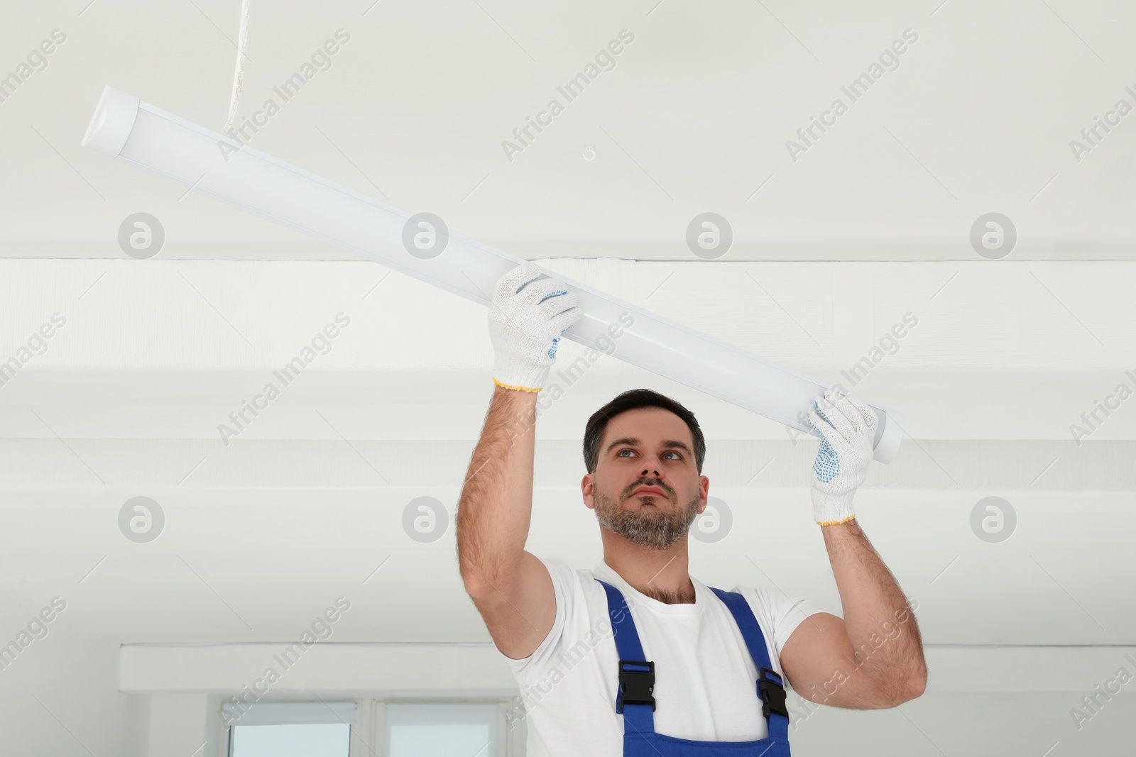 Photo of Electrician installing led linear lamp indoors. Ceiling light