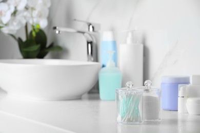 Containers with cotton swabs and pads on white countertop in bathroom. Space for text