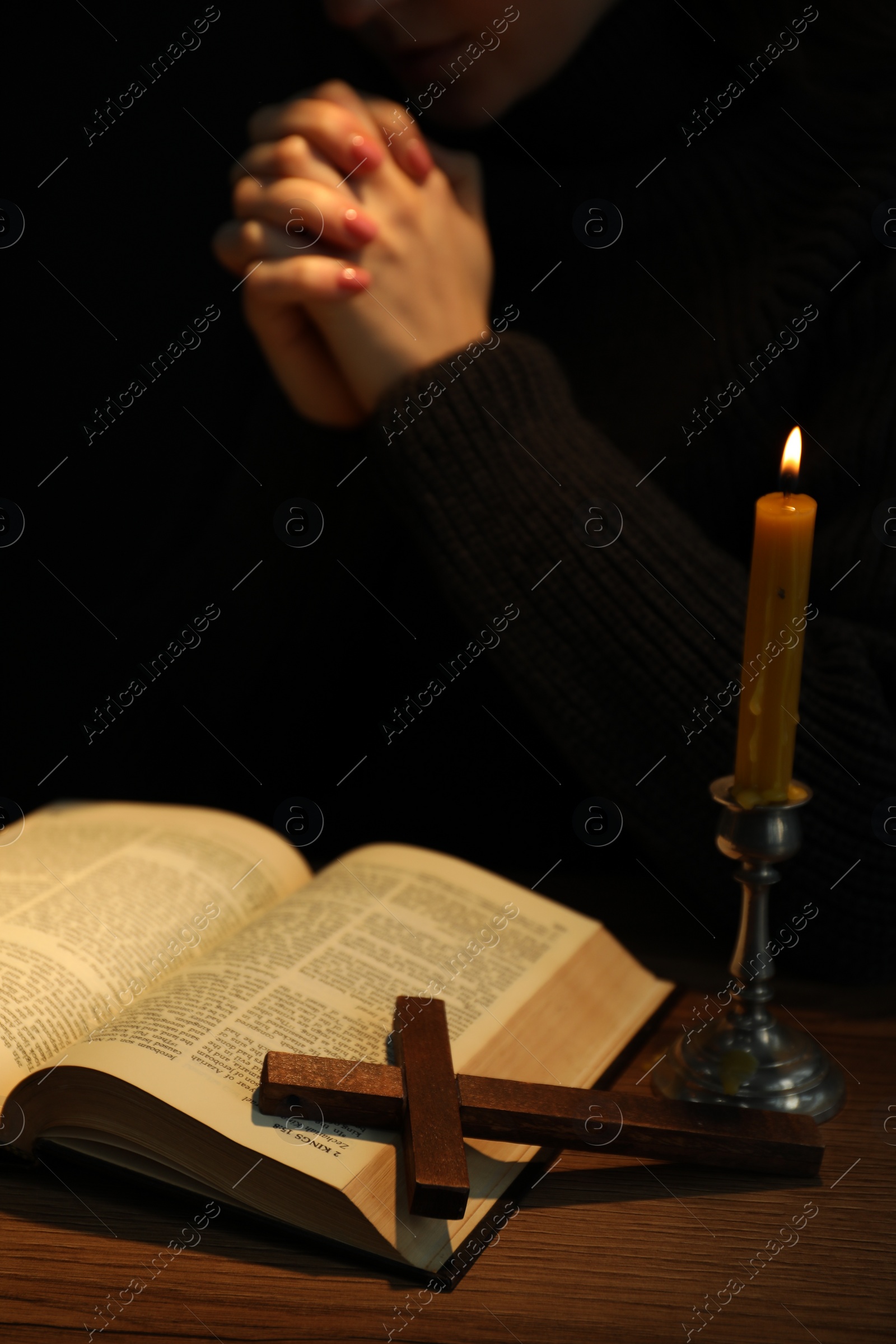 Photo of Woman praying at table with burning candle and Bible, closeup