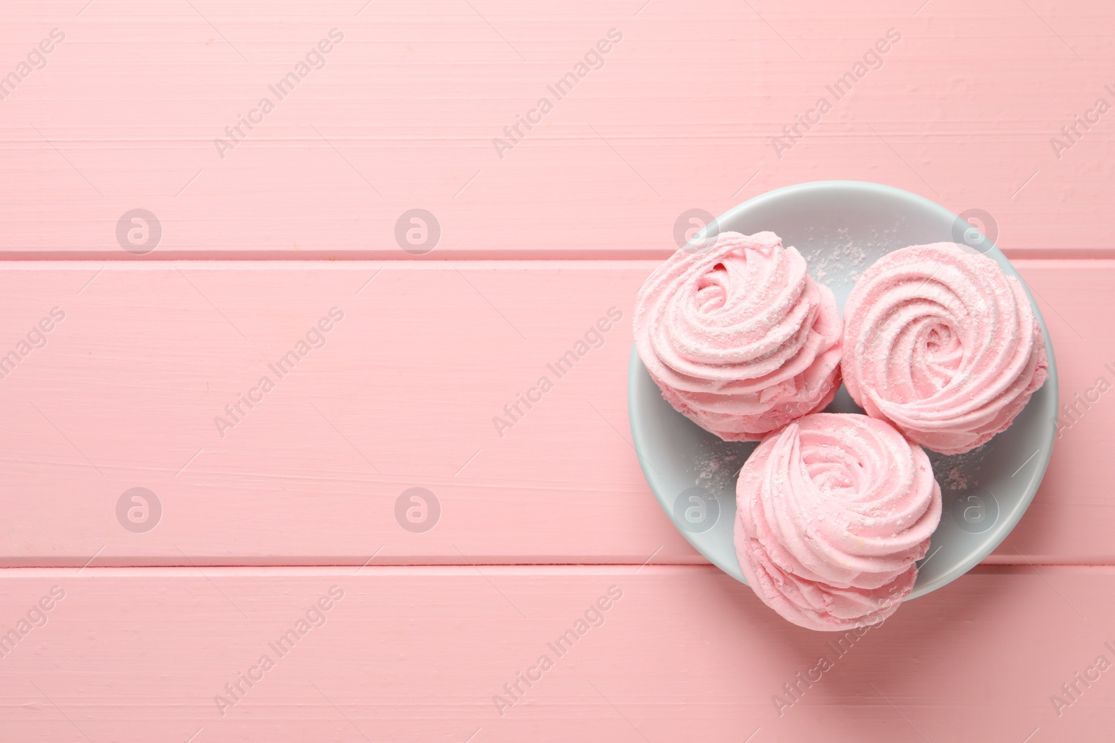 Photo of Plate with delicious zephyrs on pink wooden table, top view. Space for text