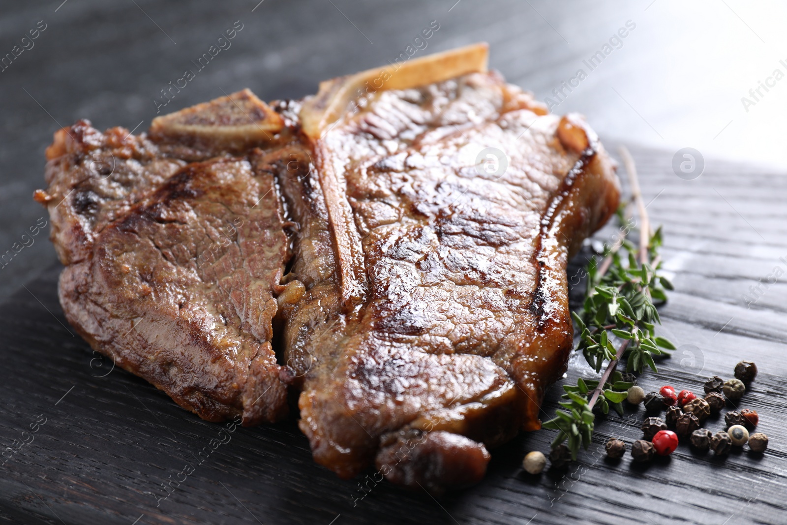 Photo of Delicious fried beef meat, thyme and peppercorns on wooden board, closeup