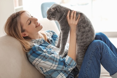 Photo of Young woman with her cute pet cat on sofa at home