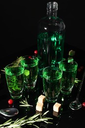 Photo of Absinthe in shot glasses, rosemary, brown sugar and spoons on mirror table. Alcoholic drink