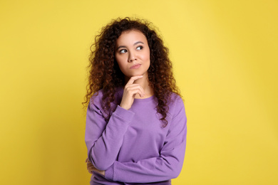 Photo of Pensive African-American woman on yellow background. Thinking about difficult question