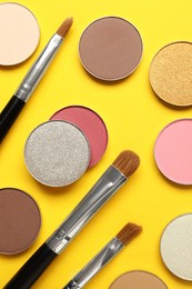Beautiful eye shadow refill pans and makeup brushes on yellow background, flat lay