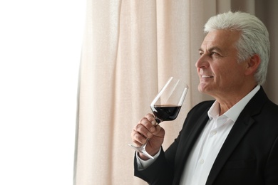 Senior man with glass of wine indoors. Space for text