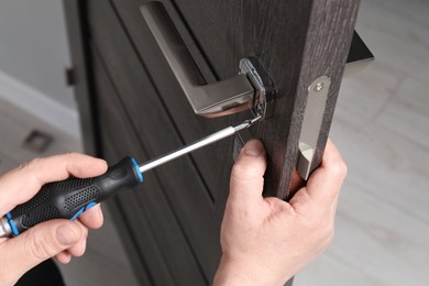 Handyman with screwdriver repairing door handle indoors, closeup