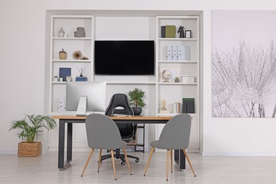 Photo of Stylish director's workplace with wooden table, tv zone, shelves and comfortable armchairs in room. Interior design