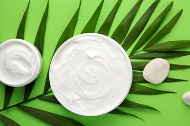 Jars of cream, leaf and stones on light green background, flat lay