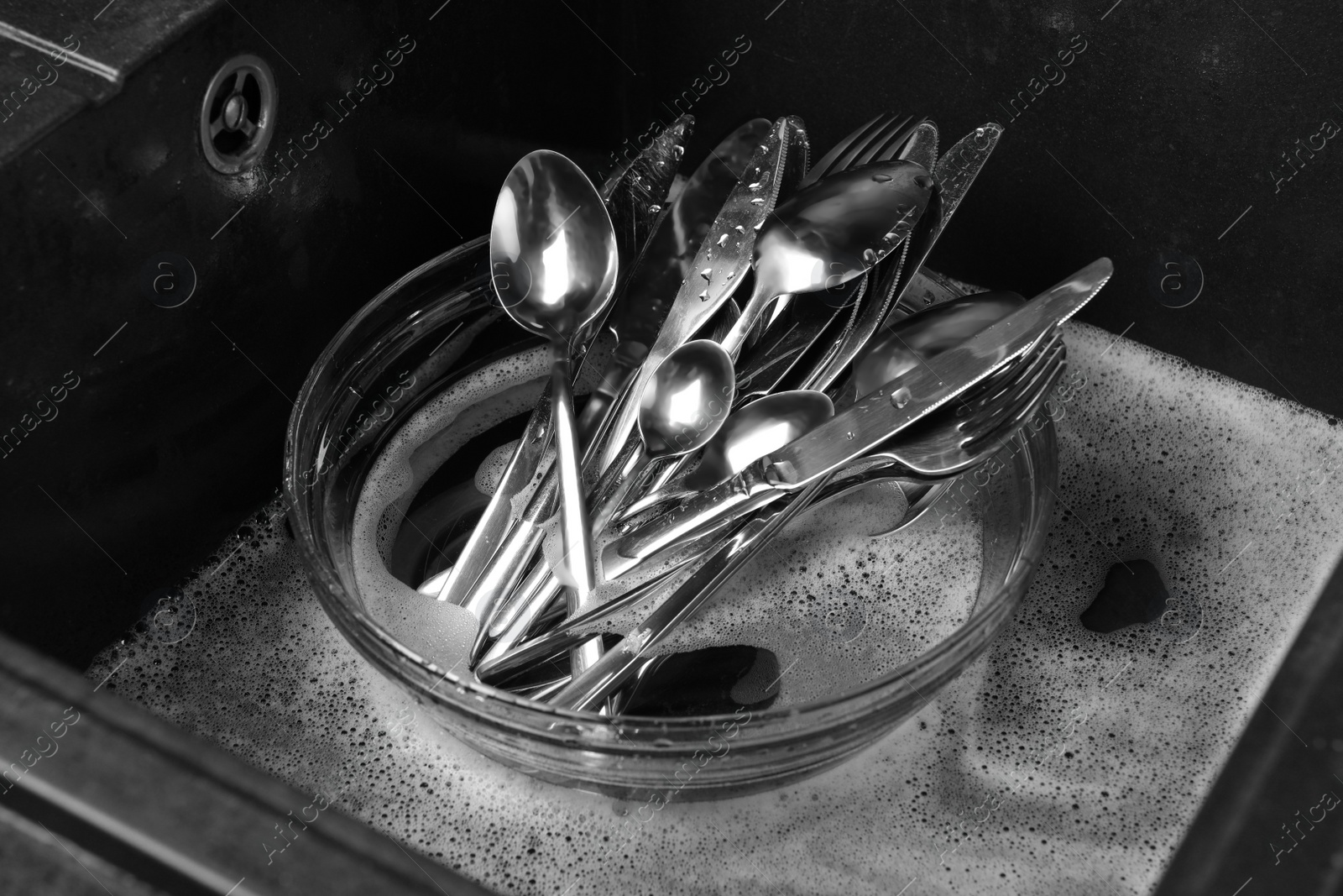 Photo of Washing silver spoons, forks and knives in kitchen sink with foam