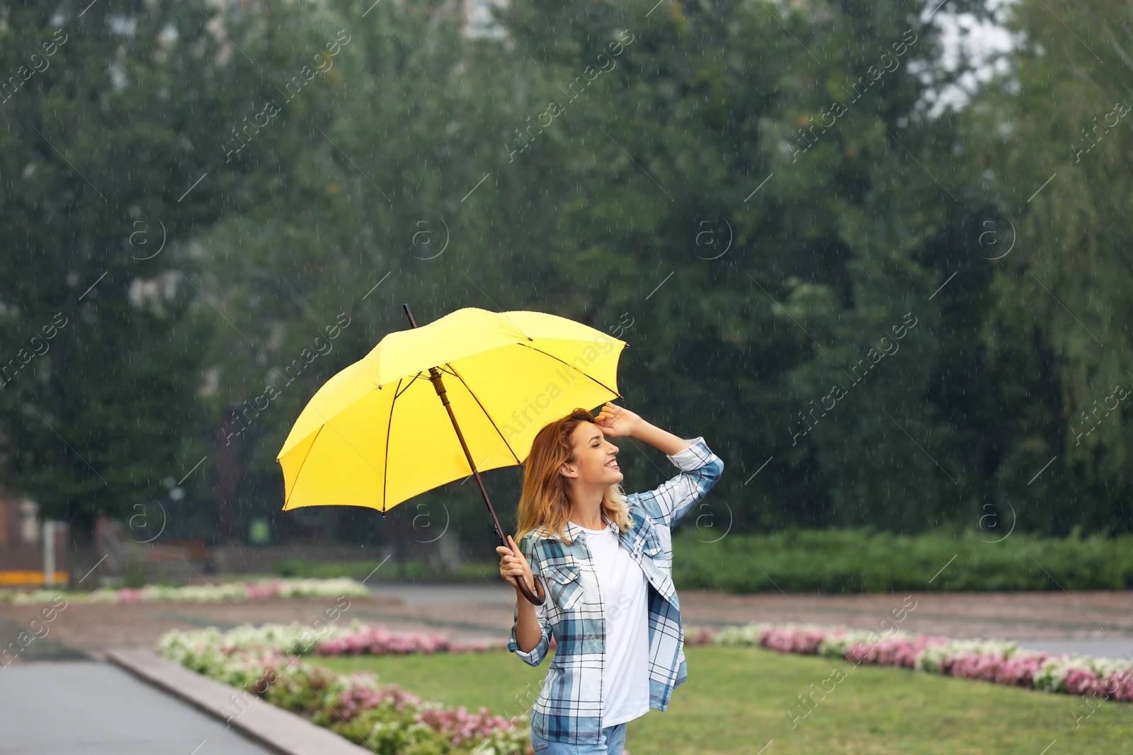 Photo of Happy young woman with umbrella under rain in park