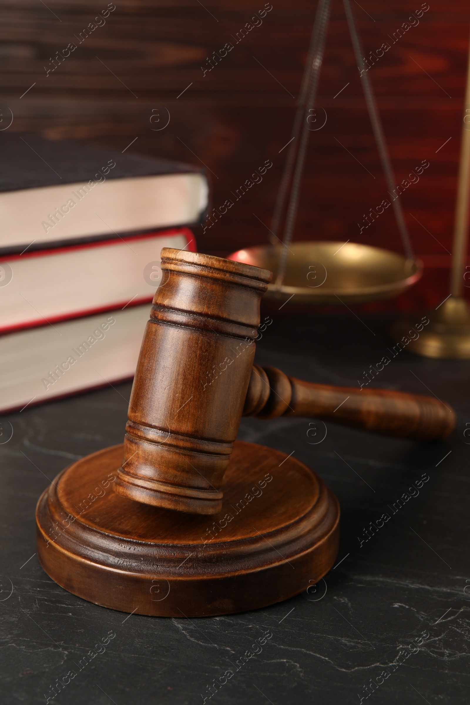 Photo of Wooden gavel, scales and stack of books on dark textured table, closeup