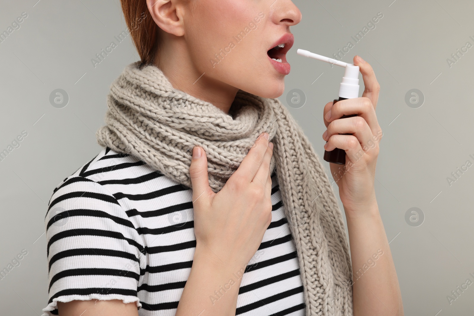 Photo of Young woman with scarf using throat spray on grey background, closeup