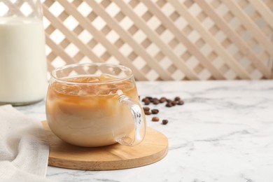 Photo of Refreshing iced coffee with milk in glass cup on white marble table, space for text