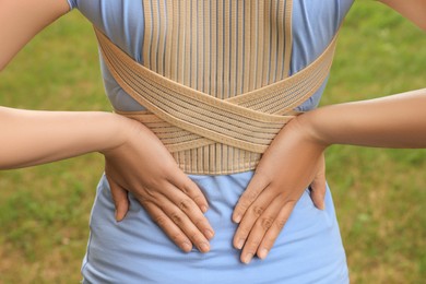 Photo of Closeup of woman with orthopedic corset on blurred background, back view