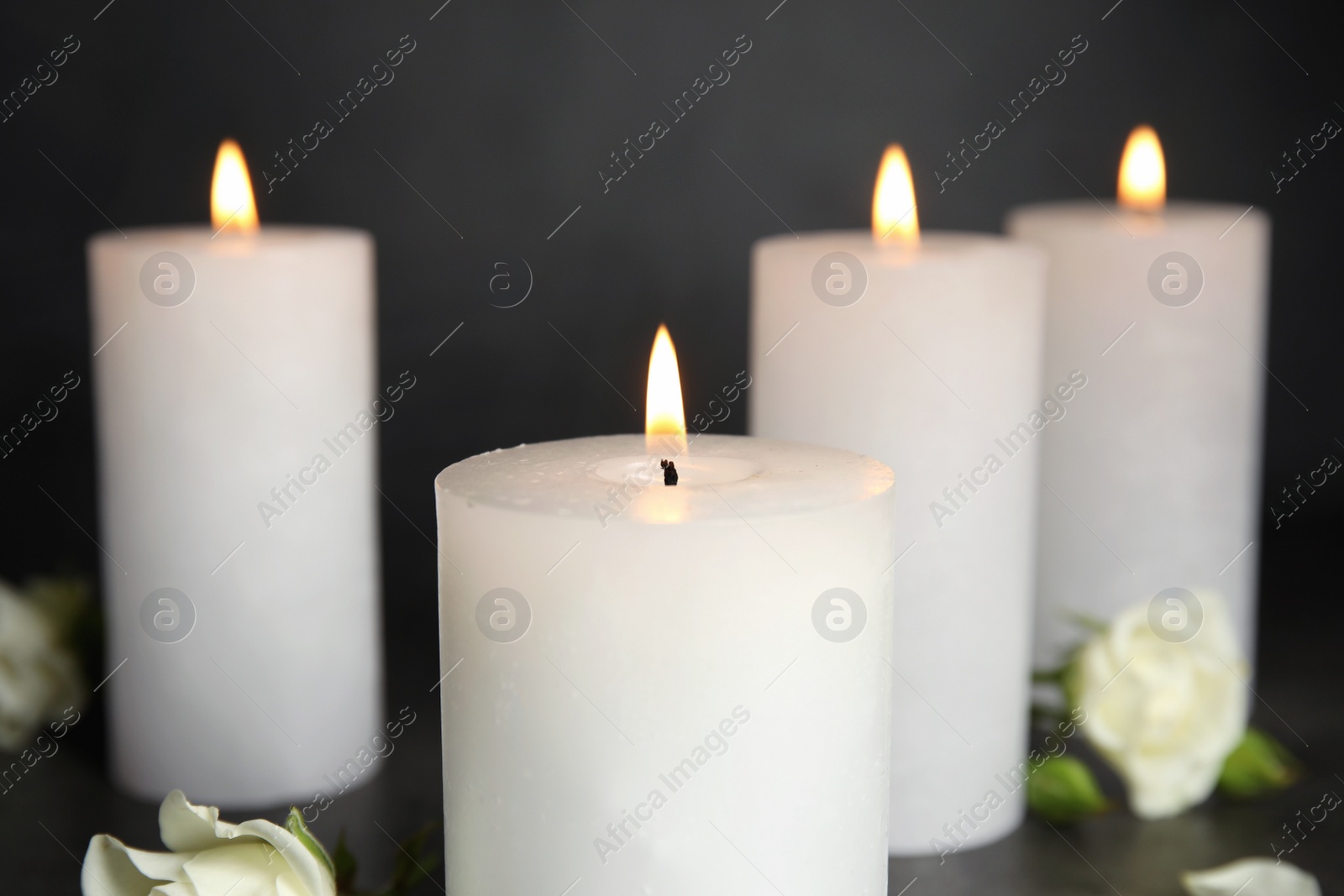 Photo of Burning candles and flowers on grey background, closeup