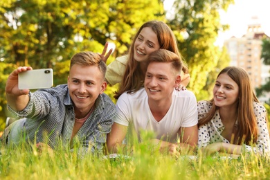 Young people taking selfie while having picnic in park on summer day