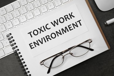 Image of Notebook with text Toxic Work Environment on black table, flat lay