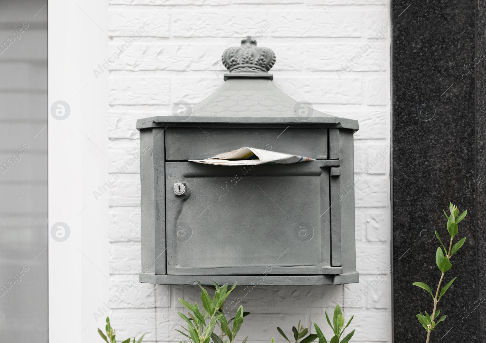 Photo of Metal letter box with newspaper on white brick wall outdoors