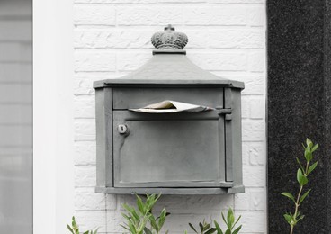 Metal letter box with newspaper on white brick wall outdoors