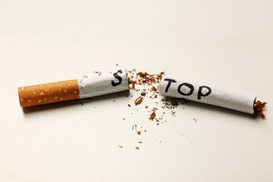Photo of Word Stop written on cut cigarette on white table, closeup. No smoking concept