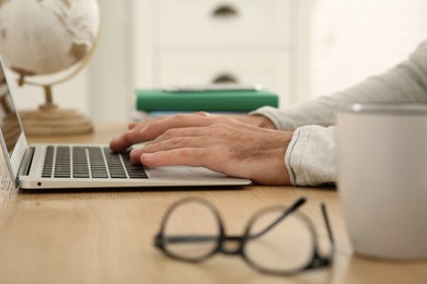 Man with laptop learning at wooden table indoors, closeup