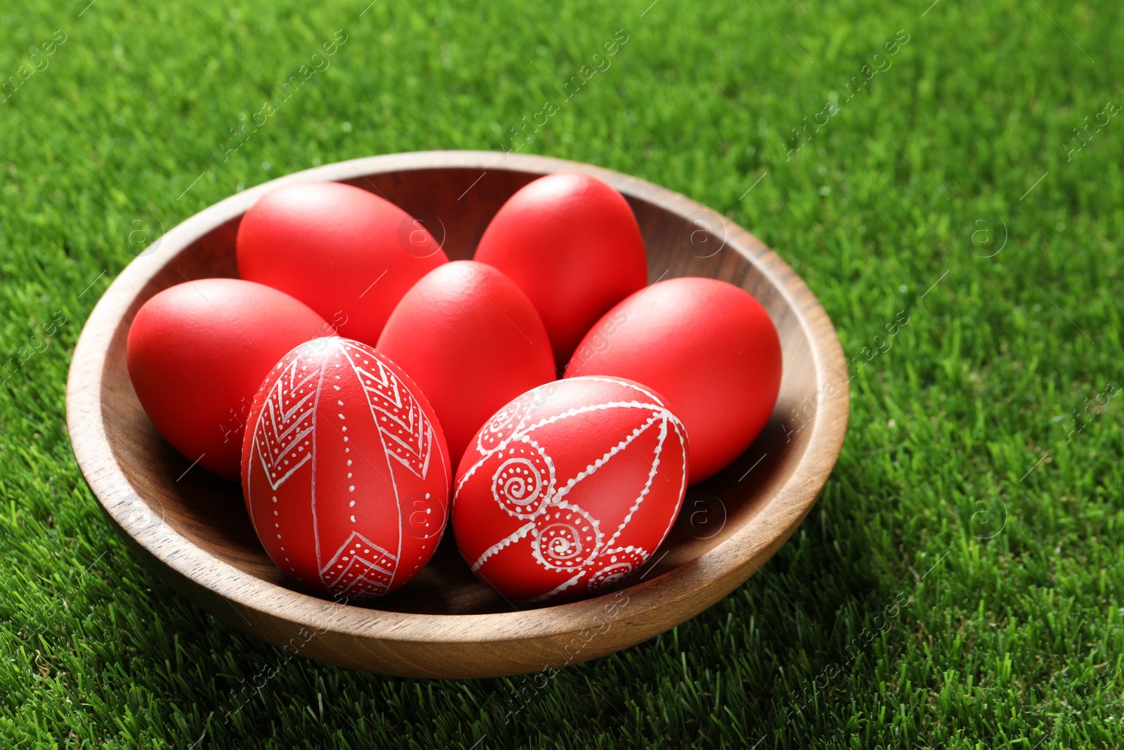 Photo of Wooden bowl with red painted Easter eggs on green grass