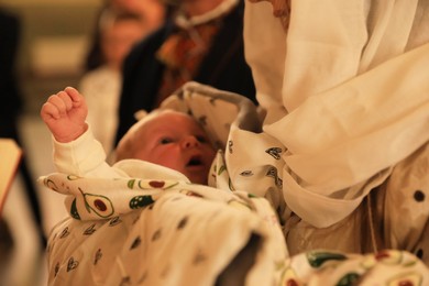 Stryi, Ukraine - September 11, 2022: Mother holding child during baptism ceremony in Assumption of Blessed Virgin Mary cathedral, closeup