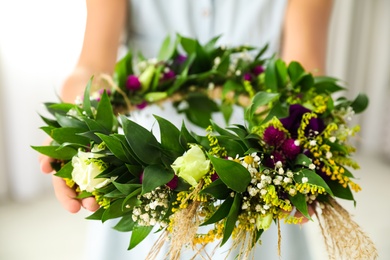 Woman holding beautiful wreath made of flowers and leaves, closeup