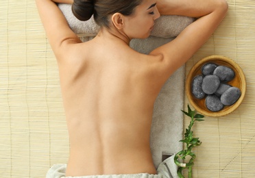 Beautiful young woman relaxing after massage on bamboo mat, top view