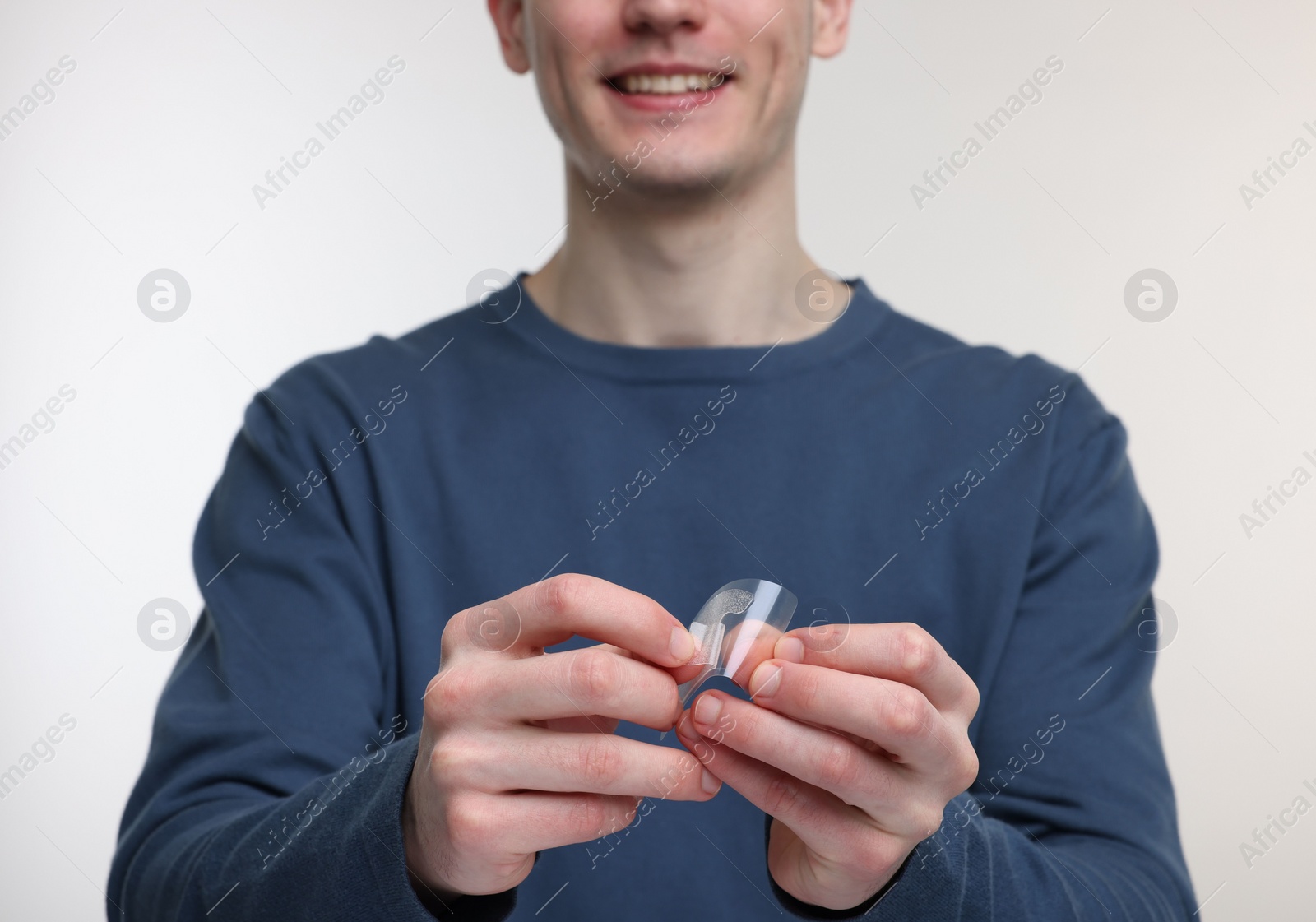 Photo of Young man with whitening strips on light background, closeup