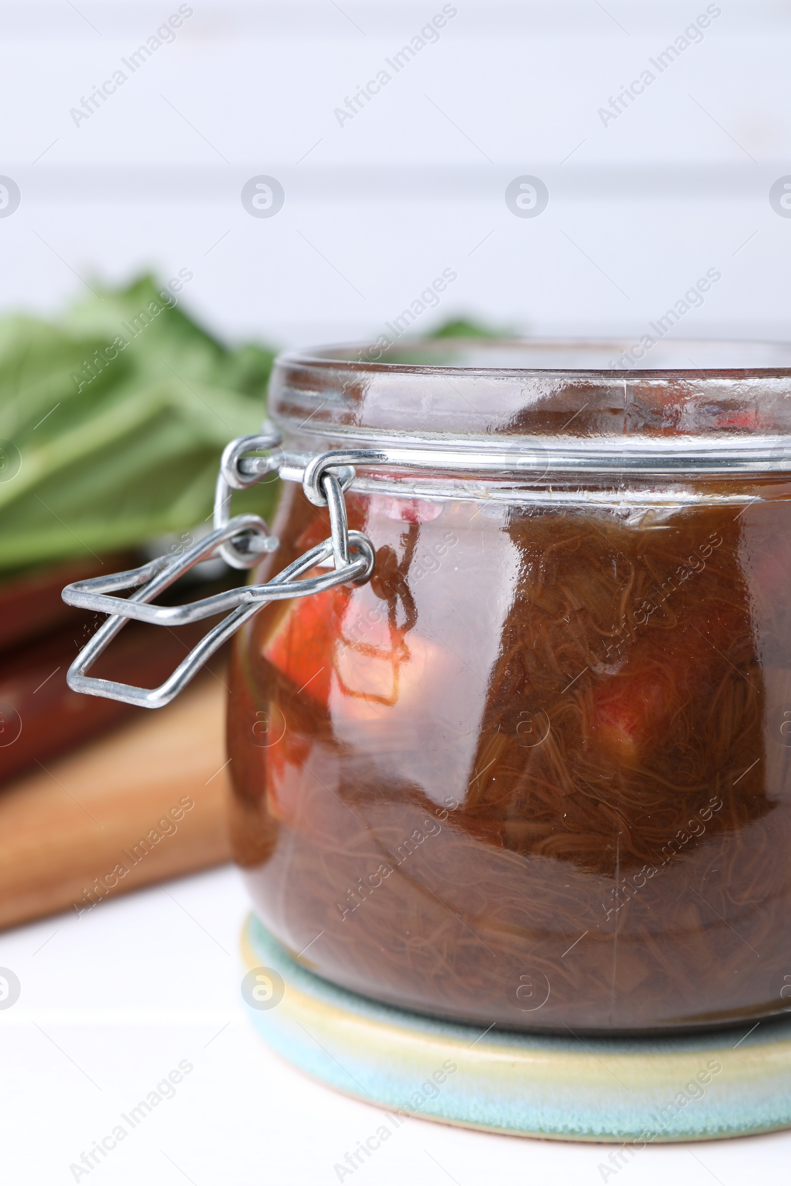 Photo of Jar of tasty rhubarb jam on white table, closeup