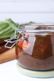 Jar of tasty rhubarb jam on white table, closeup