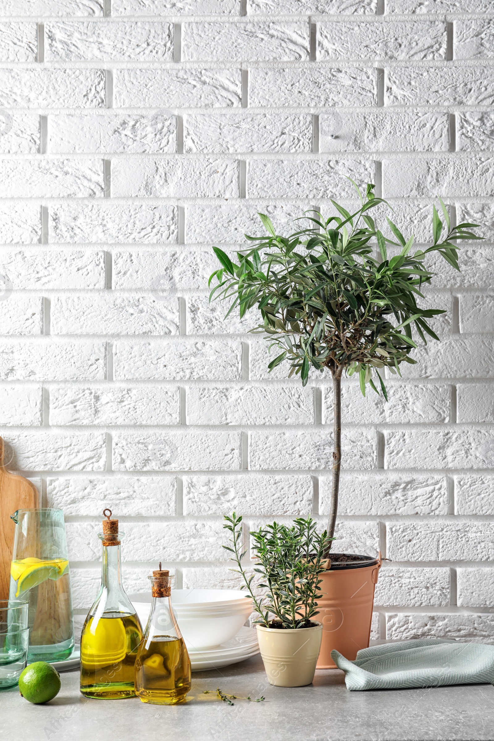 Photo of Fresh olive oil and kitchen utensils on table near brick wall