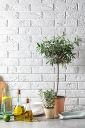 Fresh olive oil and kitchen utensils on table near brick wall