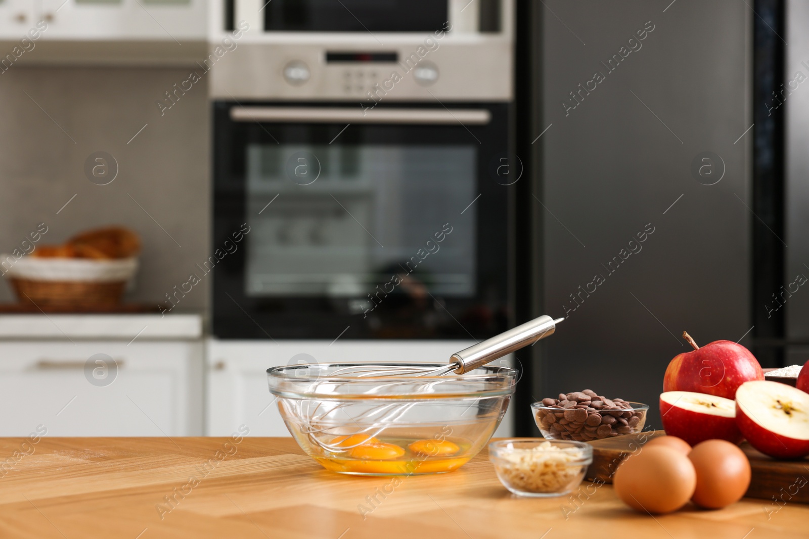Photo of Cooking process. Metal whisk, bowl and products on wooden table in kitchen. Space for text