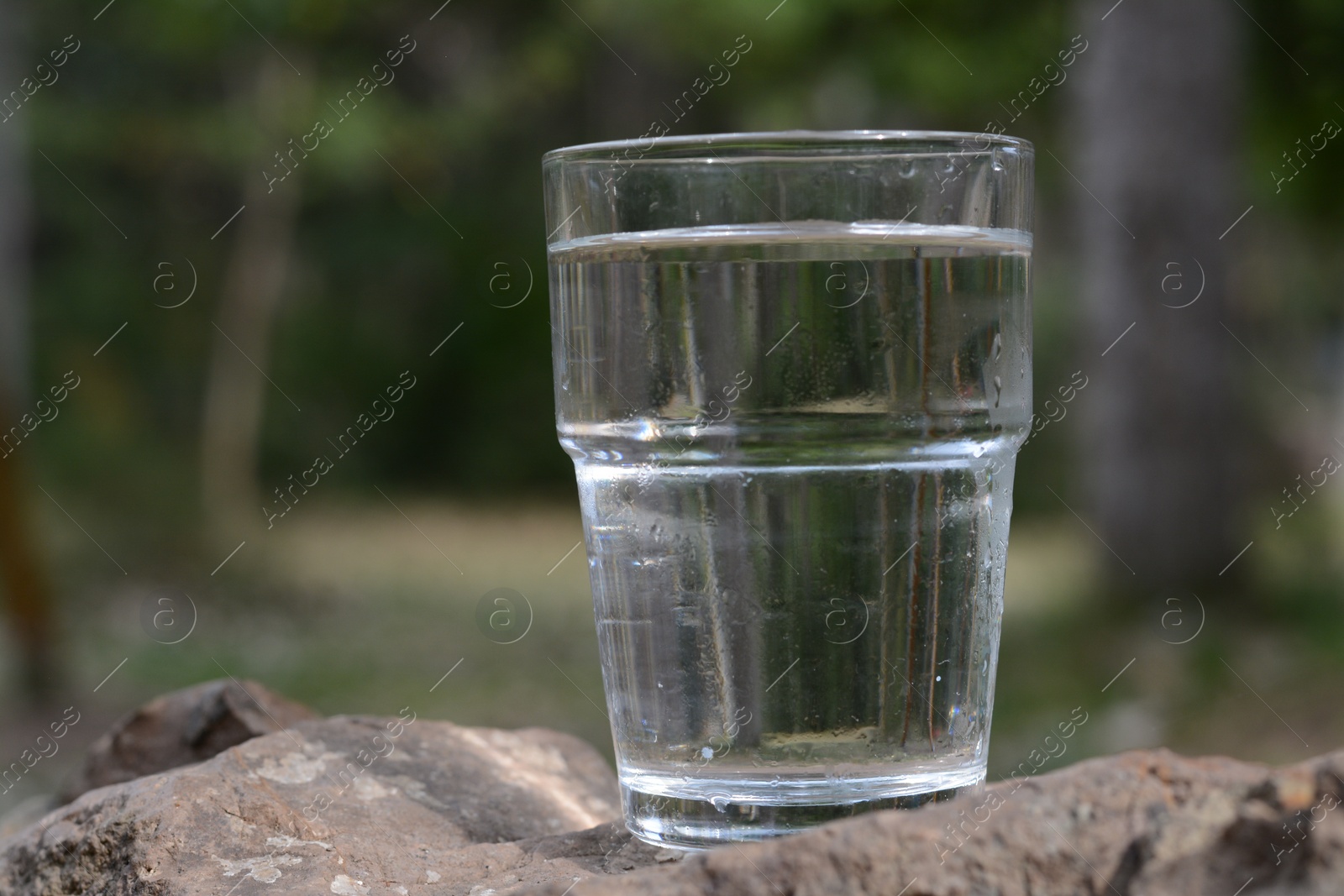 Photo of Glass of water on stone outdoors, space for text