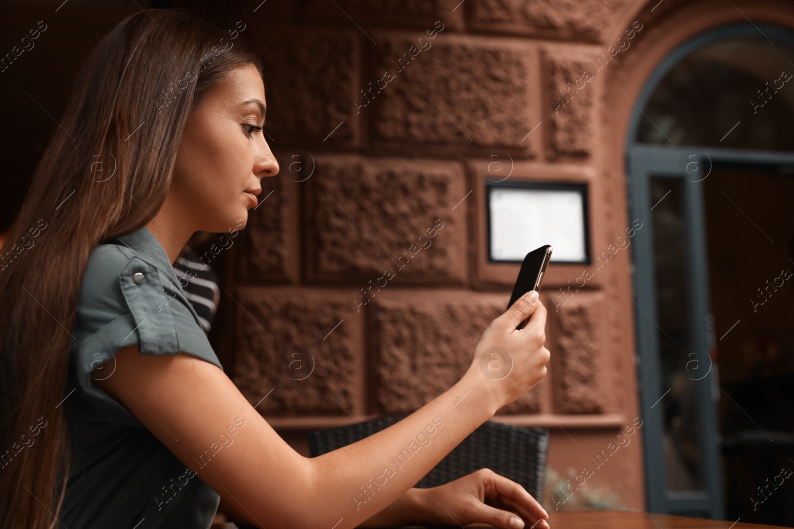 Photo of Young woman unlocking smartphone with facial scanner in outdoors cafe. Biometric verification