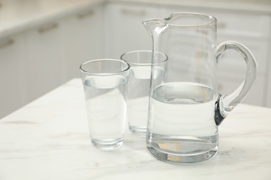 Photo of Jug and glasses with clear water on white table in kitchen