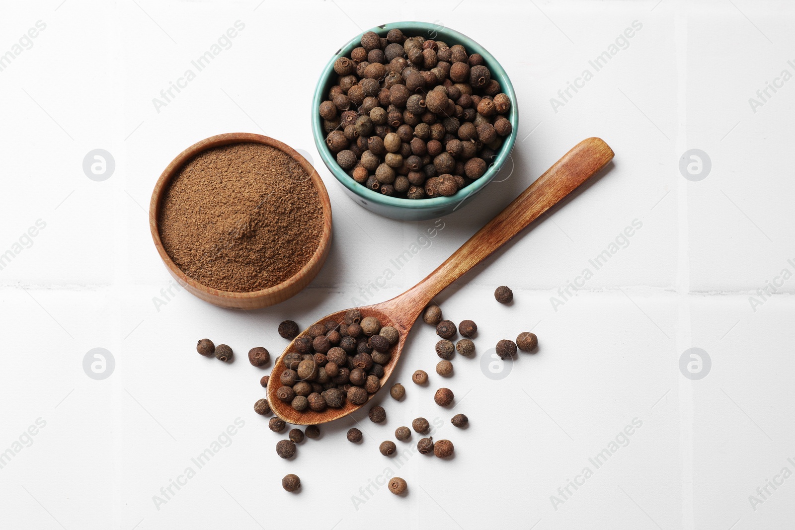 Photo of Ground and whole allspice berries (Jamaica pepper) on white tiled table, flat lay