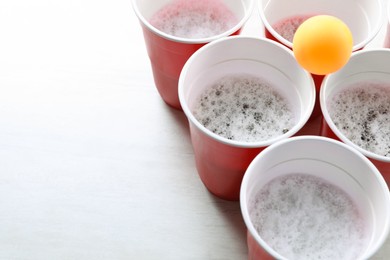 Photo of Plastic cups and ball on white table, space for text. Beer pong game