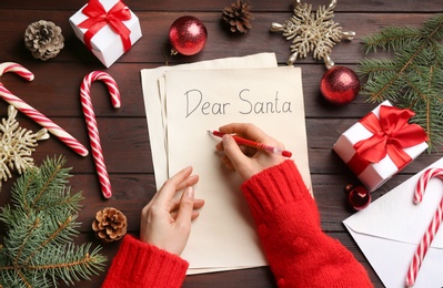 Top view of woman writing letter to Santa at wooden table, closeup