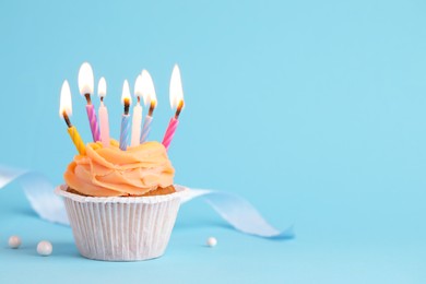 Photo of Tasty birthday cupcake with many candles on light blue background. Space for text