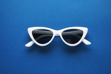 Photo of Sunglasses on bright background, top view. Color of the year 2020 (Classic blue)