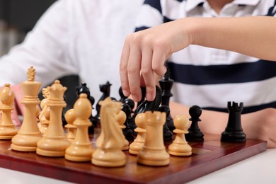 Photo of Little child playing chess at table, closeup