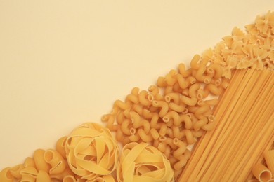 Different types of pasta on beige background, flat lay. Space for text