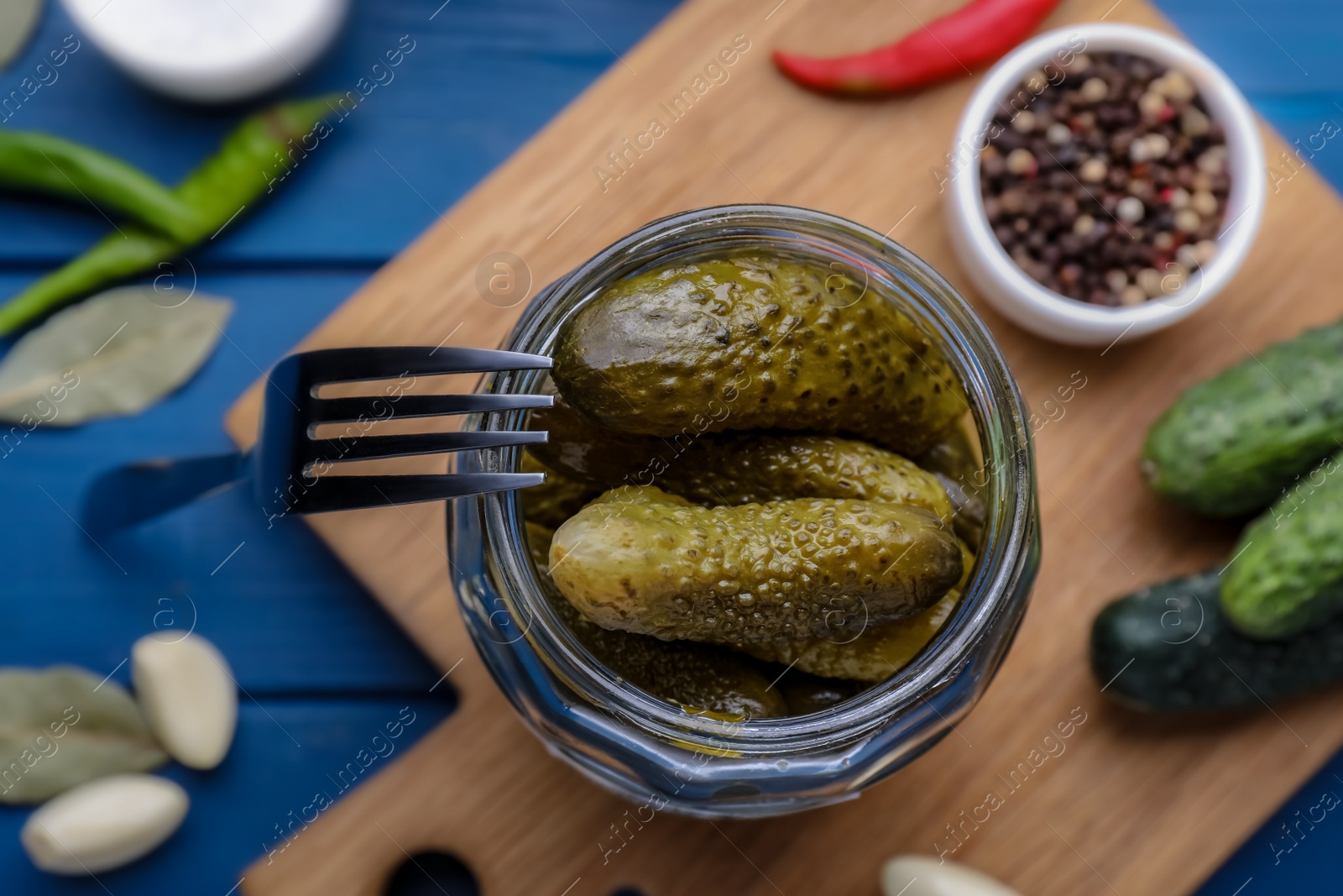 Photo of Jar of pickled cucumbers and ingredients for food preservation on blue wooden table, top view
