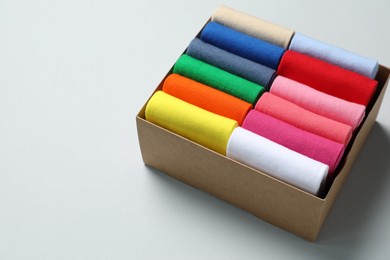 Box with different colorful socks on light background. Space for text