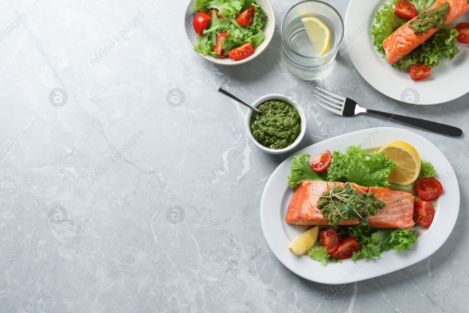 Photo of Tasty cooked salmon with pesto sauce and fresh salad on grey table, flat lay. Space for text