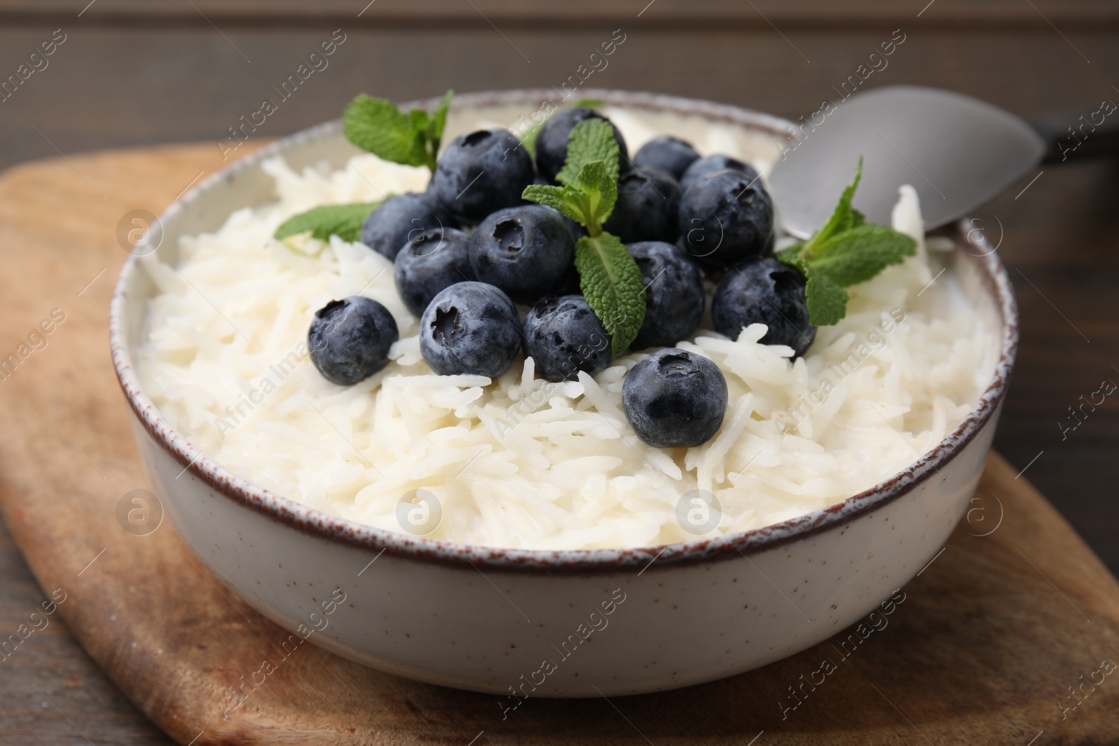 Photo of Bowl of delicious rice porridge with blueberries and mint served on table, closeup